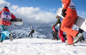 Snowboarder und Schifahrer rennen durch Schnee